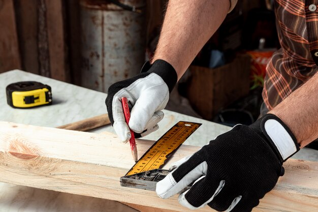 Note dell'uomo del carpentiere con una matita sui segni del bordo per il taglio, mani maschii con un primo piano della matita su un bordo di legno. carpenteria