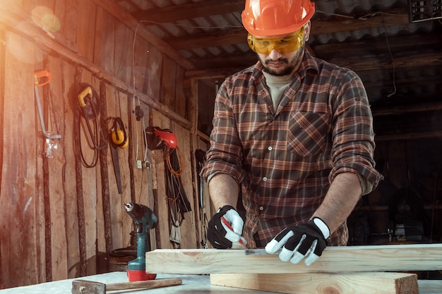 Photo carpenter man notes with a pencil on the board marks for cutting, male hands with a pencil closeup on a wooden board.