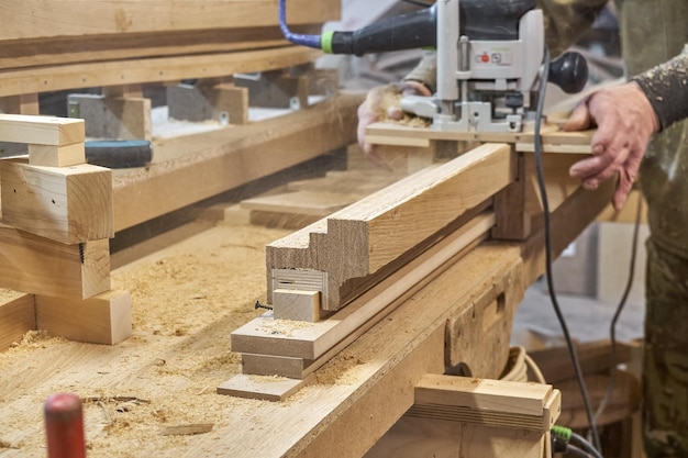 Carpenter milling wooden handrail with router manual milling machine in workshop close up