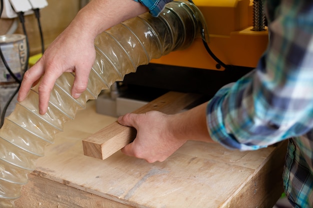 A carpenter in a plaid shirt works at a machine in a workshop. Wood. Ecological compatibility. Lifestyle. Close up. High quality photo