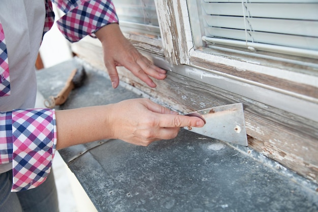 Foto falegname che rimuove lo strato di vecchia vernice dalla finestra usando la spatola