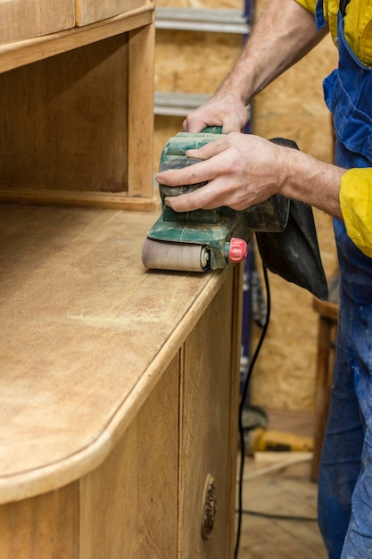 Foto carpenter restaura d'epoca il legno una credenza da un elettrico della rettificatrice.