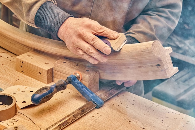 Carpenter sands bending wooden railing with sandpaper in workshop closeup