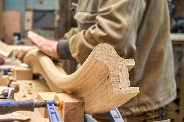 Carpenter sands bending wooden railing with sandpaper in workshop closeup