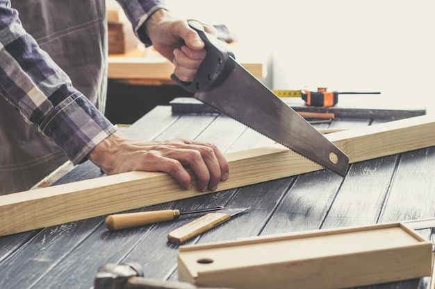 Carpenter sawing off a wooden plank in the workshop. 