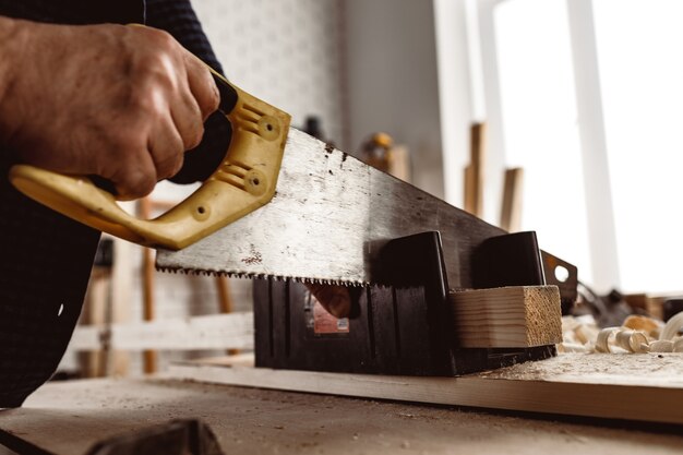 Carpenter saws a wooden block in a workshop