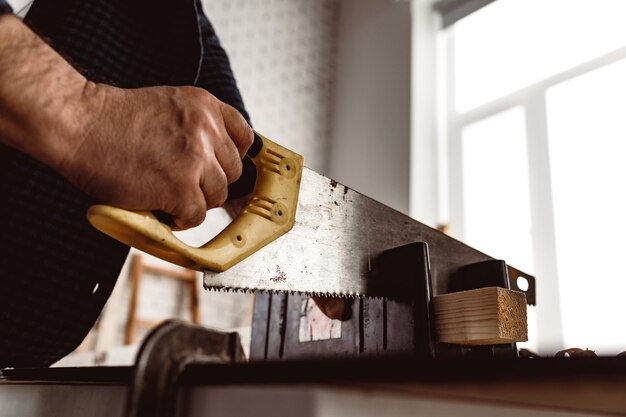 Carpenter saws a wooden block in a workshop