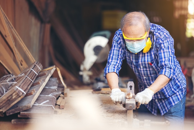 大工、作業ツールを使用して職場で木製の柵を研磨する年配の男性