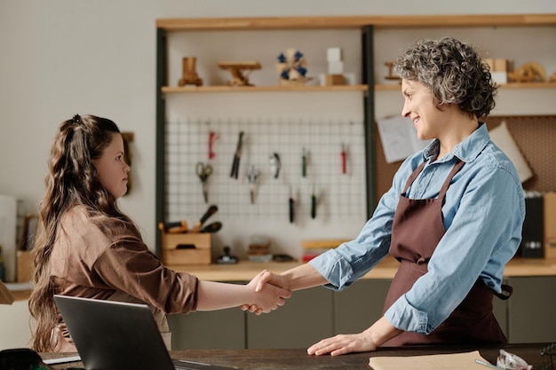 Carpenter shaking hands to girl with down syndrome while they working together in workshop