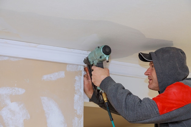 Carpenter using air nail gun to crown moldings for ceiling