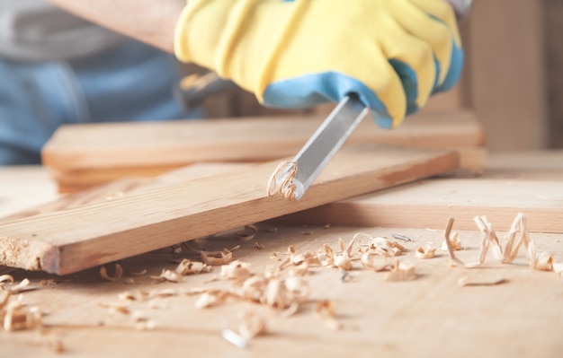 Carpenter using chisel into wooden plank.