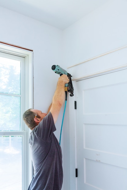 Carpenter using nail gun to moldings on door, framing trim,