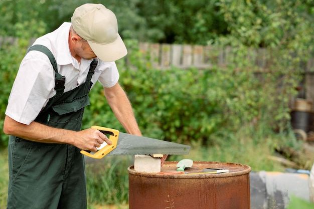 木のこぎりを使って木のシートを切る大工ワークショップで木の板を切る手のこぎりを持った大工安全工具を備えたのこぎりを使って手で大工