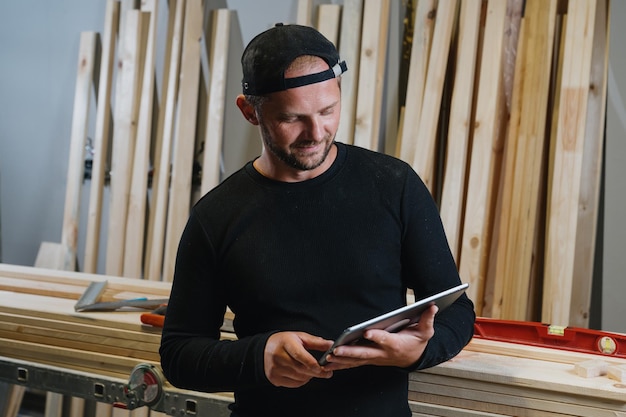Плотник с планшетом в руках на фоне мастерской Онлайн-обработка заказов