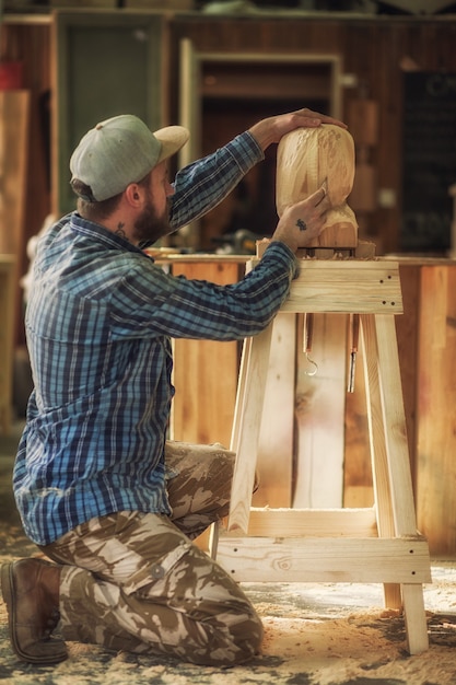 Carpenter in work clothes saw to cut out sculpture from wooden a mans head  in the workshop