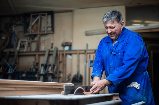 Carpentiere al lavoro nel suo laboratorio, lavorazione del legno su una macchina per la lavorazione del legno