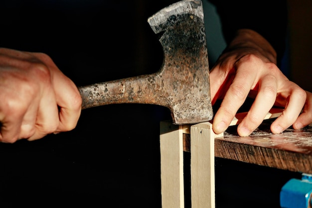 Carpenter at workbench nails down small wooden boxHands of worker with old axeAuthentic workflow in carpentry workshop