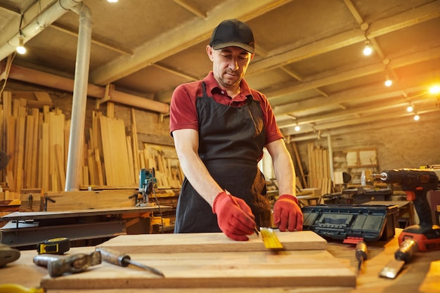 Carpenter working with a wood marking plank with a pencil and taking measurements to cut a piece of wood to make a piece of furniture in a carpentry workshop