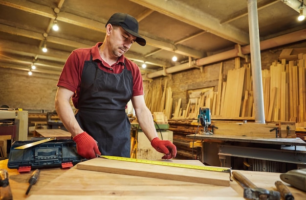 Carpenter working with a wood marking plank with a pencil and taking measurements to cut a piece of wood to make a piece of furniture in a carpentry workshop