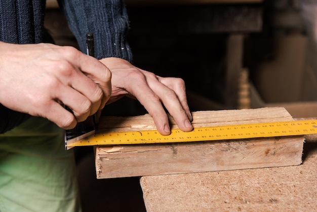 A carpenter works in a furniture workshop with various tools and a board