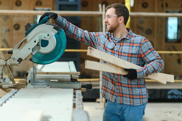 A carpenter works on woodworking the machine tool Man collects furniture boxes Saws furniture details with a circular saw Process of sawing parts in parts Against the background of the workshop