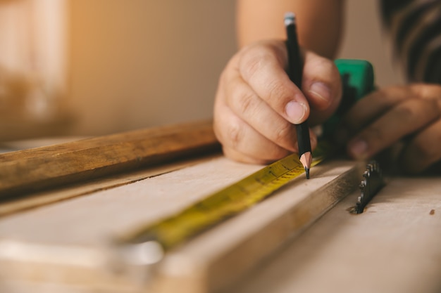 Carpenter in the workshop marks on wooden board in workshop