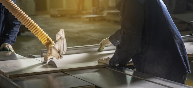 Carpenter in the workshop saws chipboard and a wooden board with a circular saw on the machine