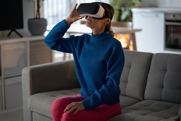 VR 및 AR을 사용하여 올려다보는 가상 현실 헤드셋을 착용한 유럽 여성이 소파에 앉아 있습니다.