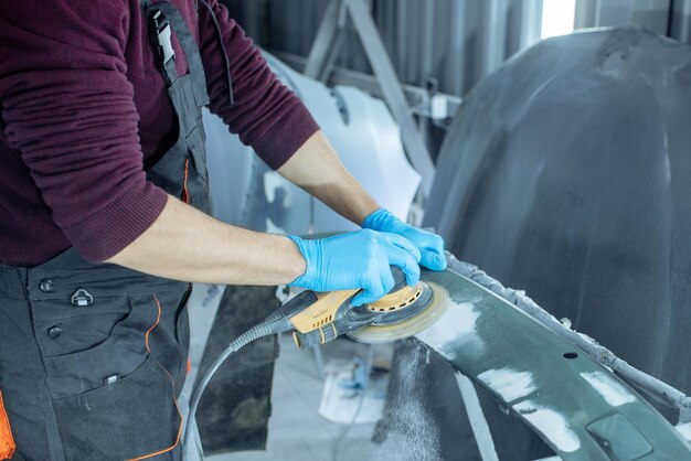 Carrosserie repareren door dichtwerk na het ongeval te plamuren door schuurprimer te werken vóór het schilderen. , De monteur repareert de auto , Plastic stopverf gebruiken , Oppervlak voorbereiden voor verfspuiten.