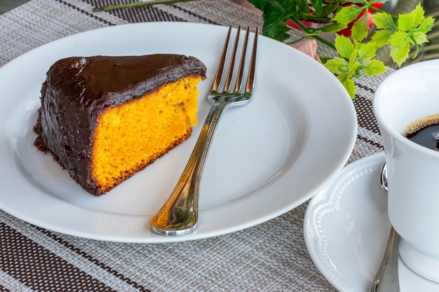 Photo carrot cake with chocolate icing, accompanied by a cup of coffee.