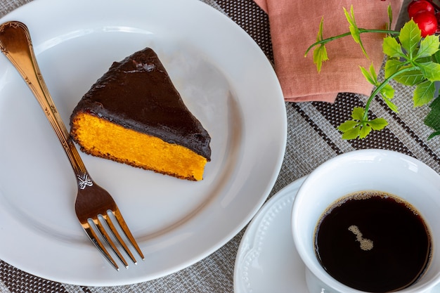 Carrot cake with chocolate icing, accompanied by a cup of coffee.