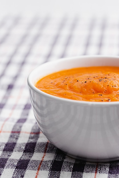 Carrot cream soup in a white bowl with cloth napkin