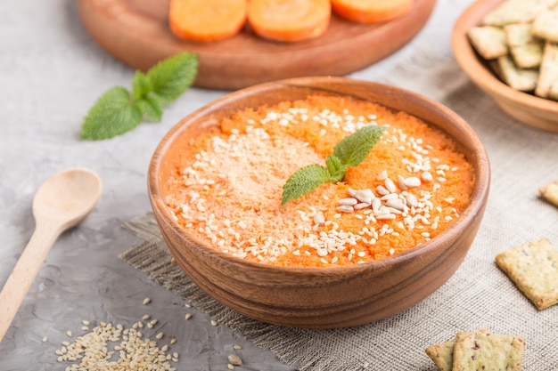 Carrot cream soup with sesame seeds and snacks in wooden bowl on a gray concrete background. side view, selective focus.