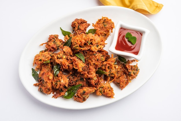 Carrot Fritters or Gajar ke pakore or pakode or bajji or bhaji, Indian snack served in a plate with tomato ketchup