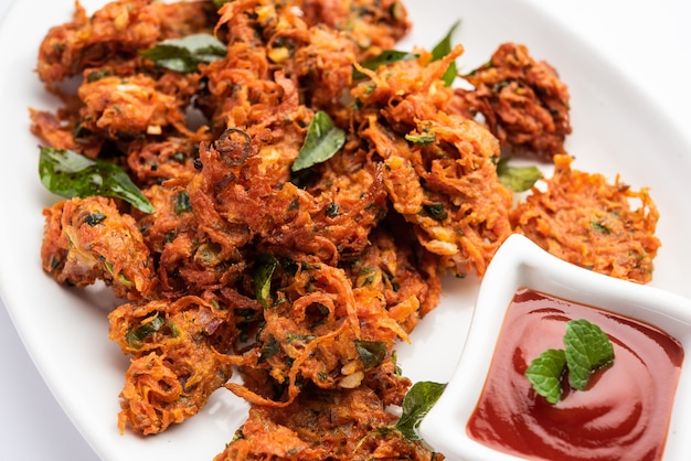 Carrot Fritters or Gajar ke pakore or pakode or bajji or bhaji, Indian snack served in a plate with tomato ketchup