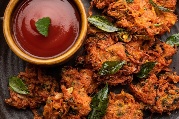 Carrot Fritters or Gajar ke pakore or pakode or bajji or bhaji, Indian snack served in a plate with tomato ketchup