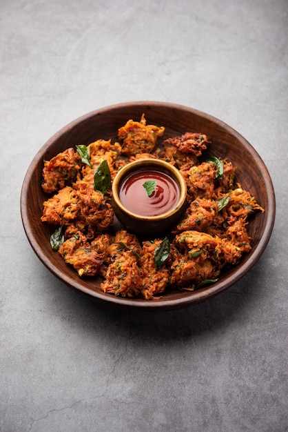 Carrot Fritters or Gajar ke pakore or pakode or bajji or bhaji, Indian snack served in a plate with tomato ketchup