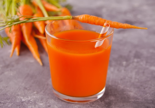Морковный сок и молодая морковь в стакане на бетонном фоне