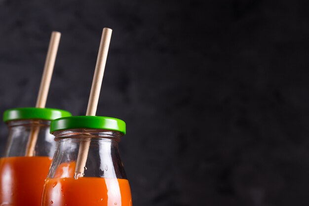 Carrot and orange juice in glass bottles with eco straws in low key close up