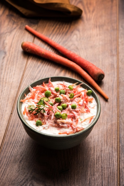 Carrot raita OR Gajar Koshimbir with Curd, green, peas, chillies and coriander. Served in a bowl over moody background. selective focus