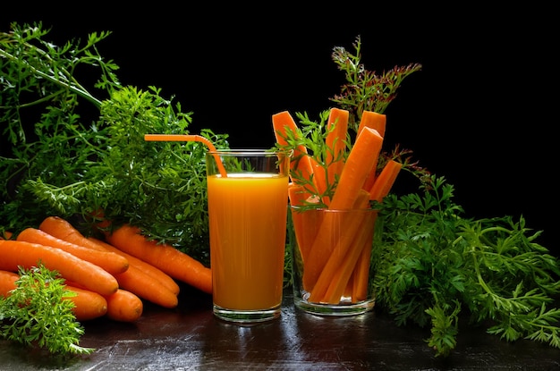 Carrot root and juice in glass with foliage on black stone background Healthy lifestyle diet food