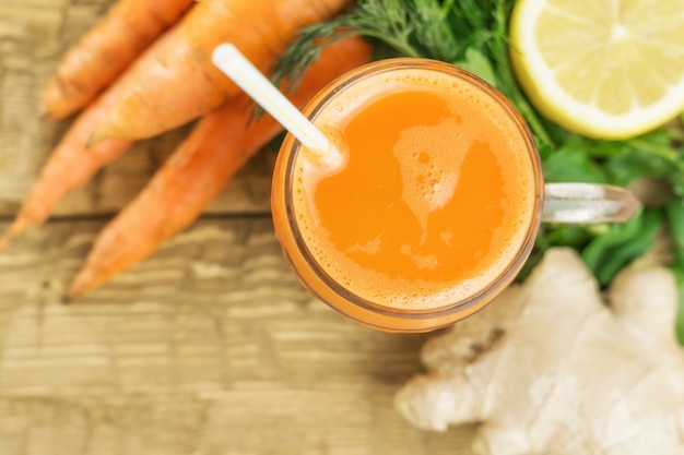 Carrot smoothie with ginger root and lemon on a wooden table.