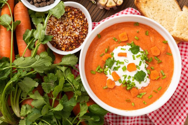 Carrot soup of freshly ground carrots with herbs and sour cream on a wooden table.