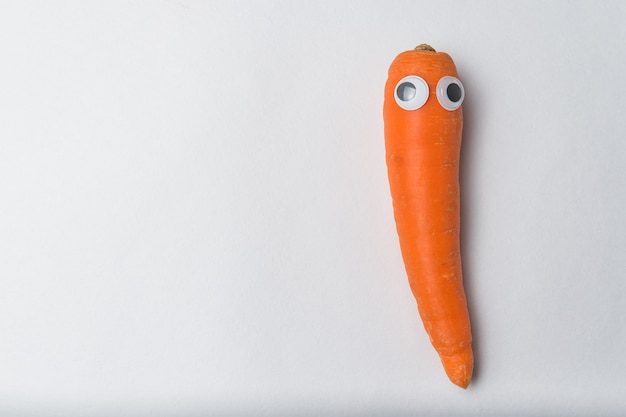 Carrot with funny face and Googly eyes on white wall. Vegetarianism concept