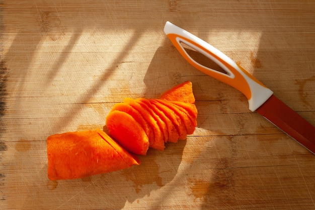 Carrots cut into pieces and an orange knife on a wooden board with a shadow