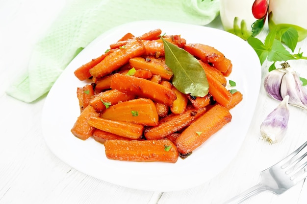 Морковь жареная в тарелке на светлой деревянной доске
