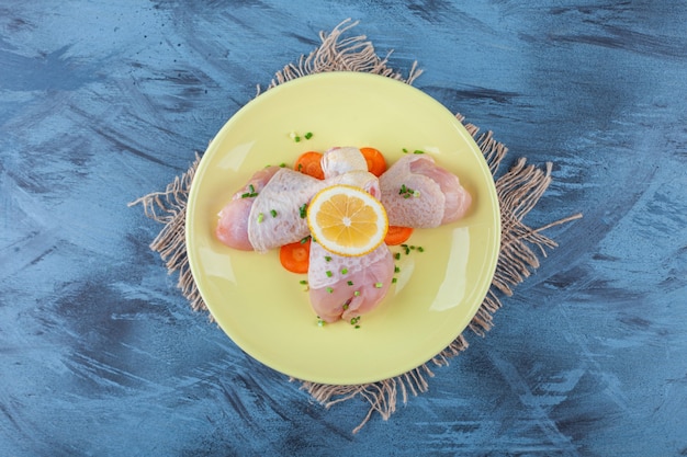 Carrots lemon and drumsticks on a plate on a burlap napkin, on the blue surface.