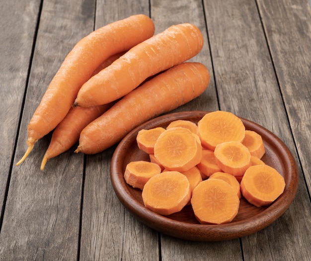 Photo carrots and slices on a plate over wooden table.