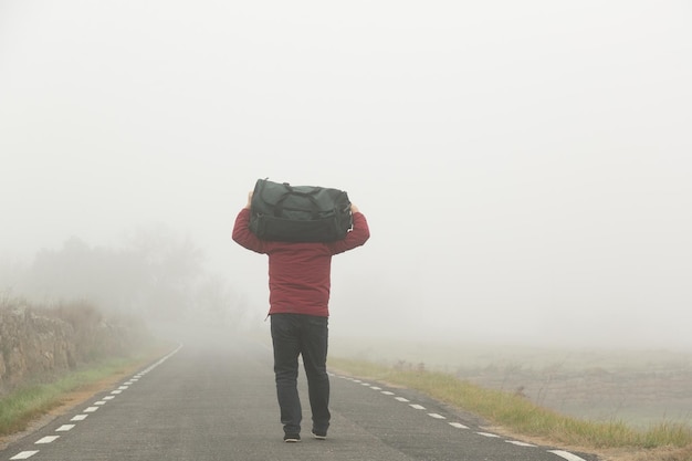 Photo carrying a suitcase in his arms an unrecognizable man walking along a road on a foggy day