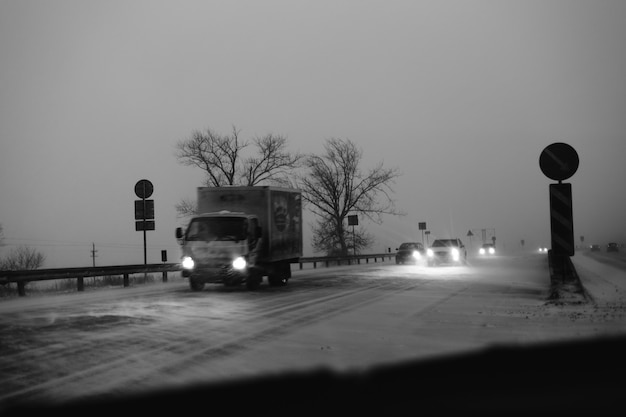 Cars drive on the highway during a snowstorm in the evening.